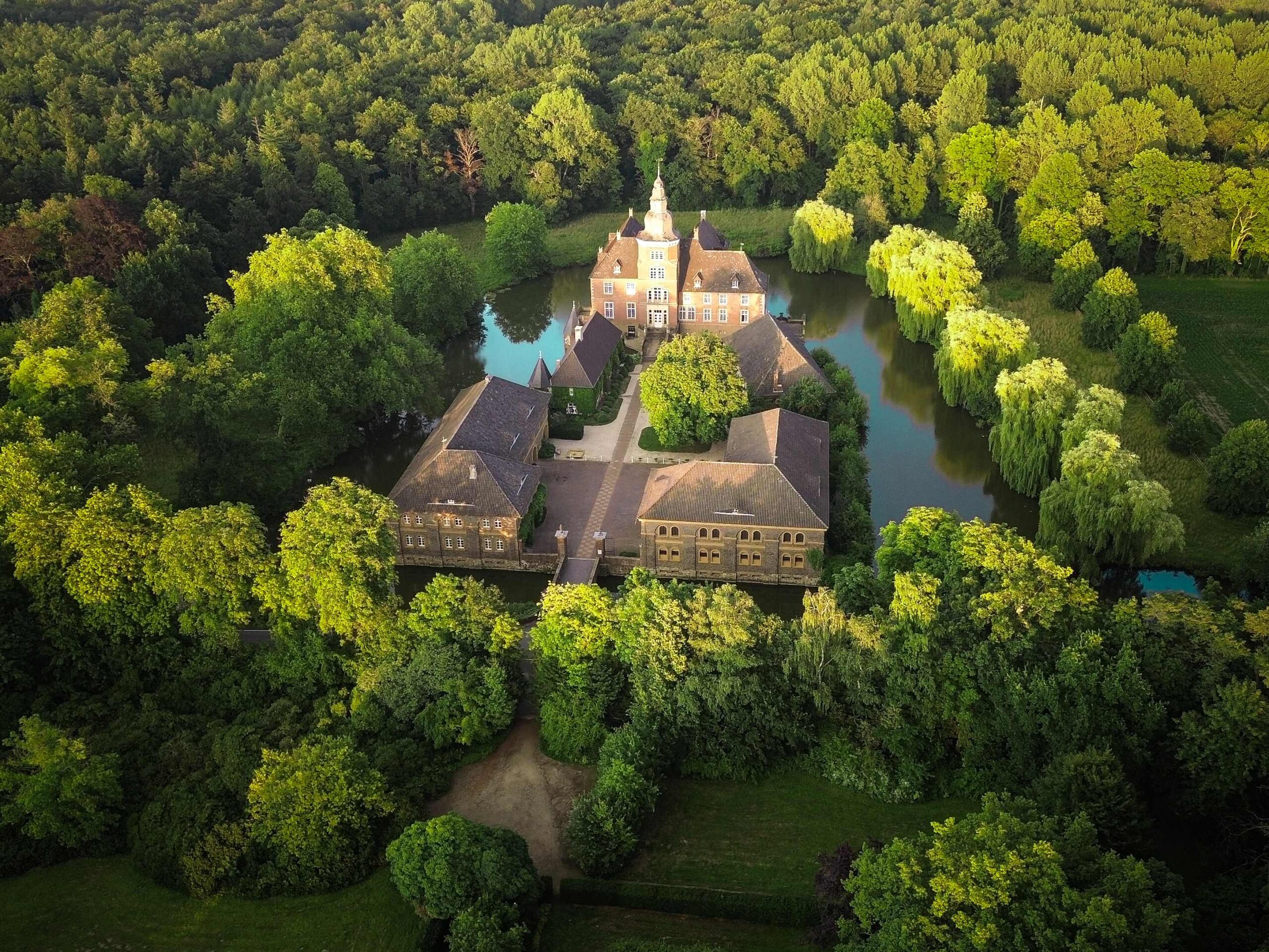 Luftaufnahme des Wasserschlosses Sandfort, umgeben von Wassergräben und eingebettet in grüne Landschaft, ein historisches Bauwerk in idyllischer Naturkulisse.