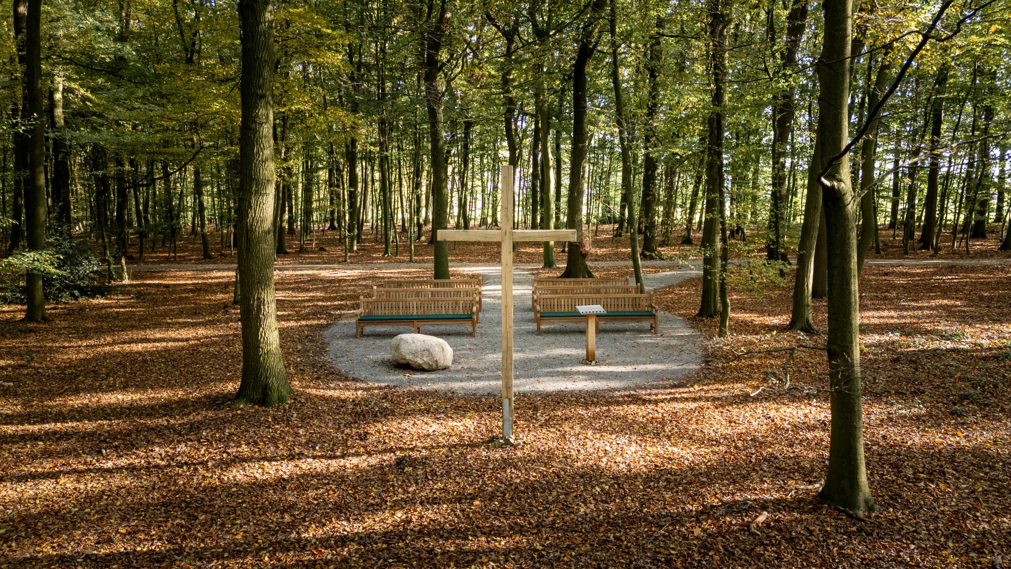 Andachtsplatz mit Holzkreuz und Bänken im herbstlichen Ruhewald Sandfort, umgeben von Bäumen.